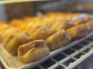 A tray of glazed donuts on a metal rack, with more donuts visible in the background.